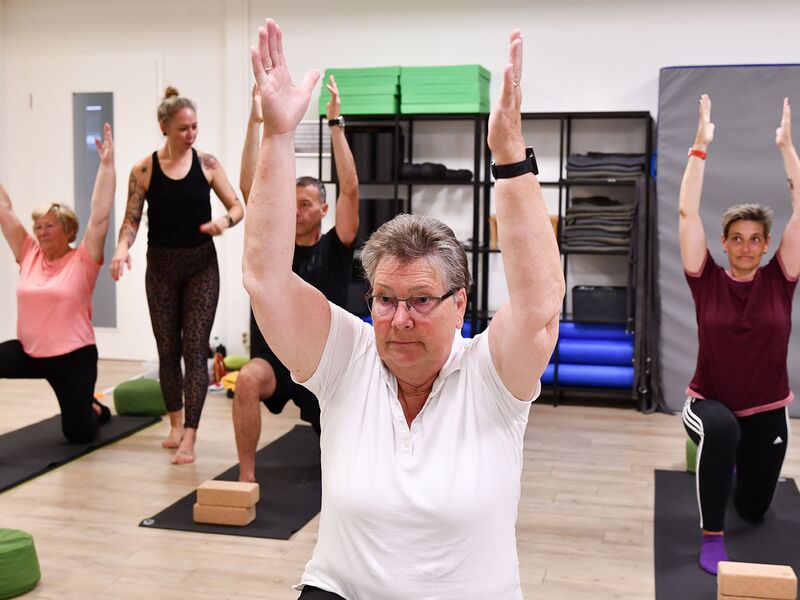 4 Personen die eine Yogapose halten mit Anleitung der Kursleitung